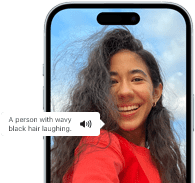 iPhone 15 s aktívnou funkciou Voiceover, ktorá popisuje obrázok smejúcej sa osoby s vlnitými čiernymi vlasmi