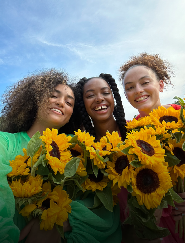 Ostré a zářivě barevné selfíčko tří lidí, kteří drží květiny.