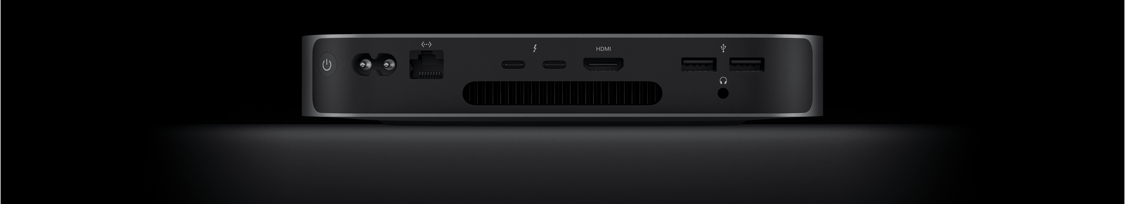 Pohled zezadu na Mac mini s viditelnými dvěma porty Thunderbolt 4, portem HDMI, dvěma porty USB‑A, sluchátkovým konektorem, portem gigabitového ethernetu, napájecím portem a tlačítkem napájení.